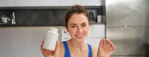 Close up portrait beautiful smiling fitness woman showing vitamin bottle with dietary supplement